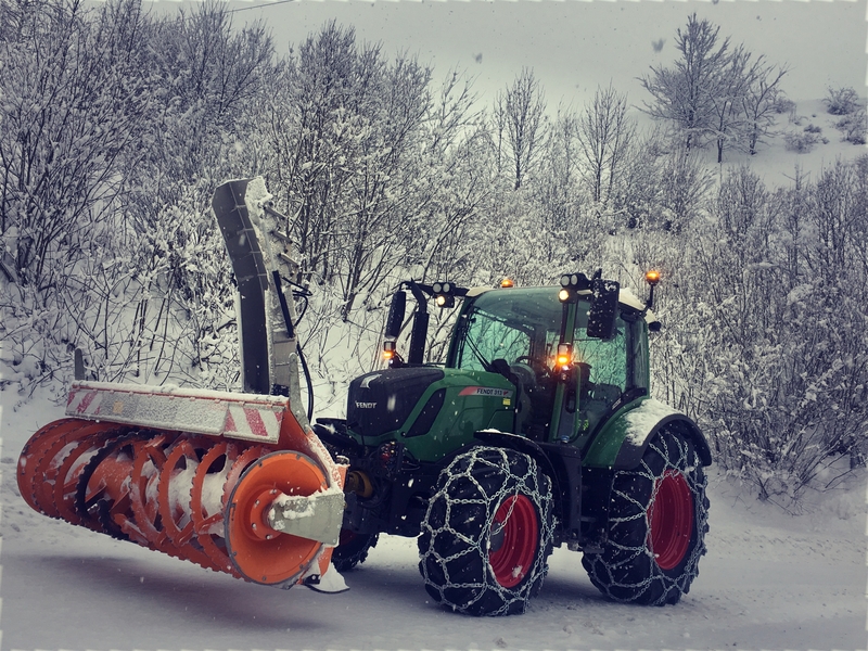 Traktor mit Schneefräse im Wald, dichte Schneedecke bedeckt die Bäume und den Boden.