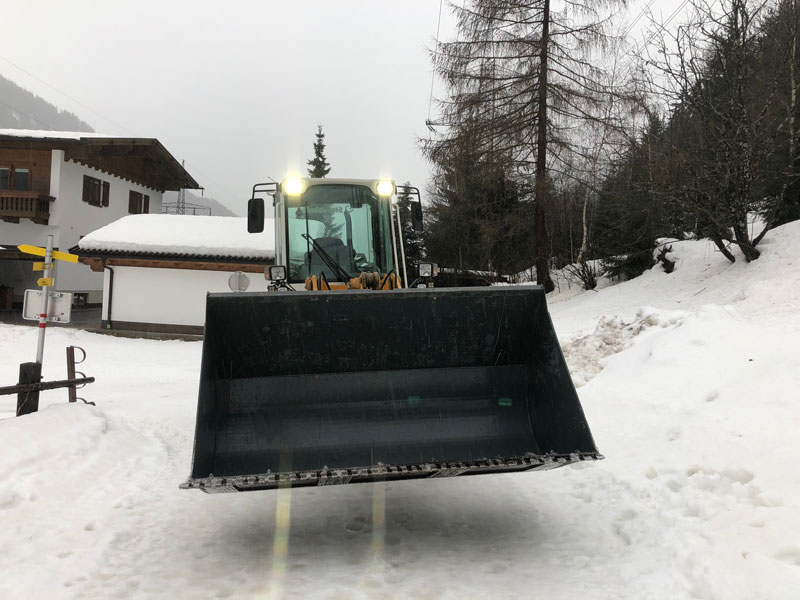 Großer Radlader mit Schneeschaufel beim Schneeräumen auf winterlicher Bergstraße rund um St. Anton am Arlberg.